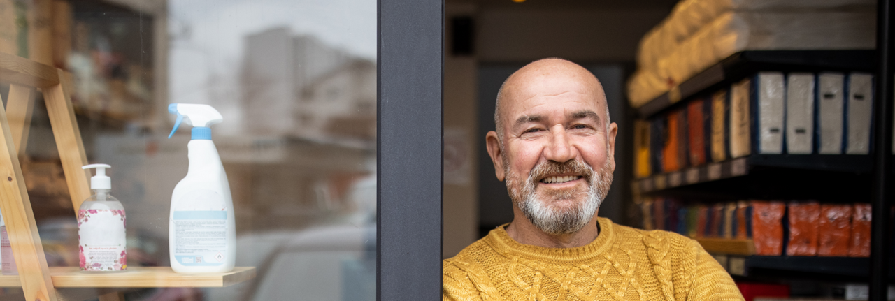 Image d’un homme souriant en pull orange avec les bras croisés sur le pas d’une porte